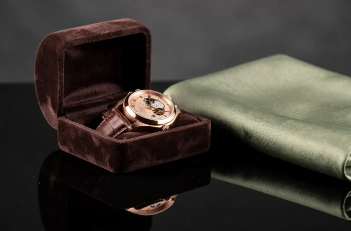 Composition de luxe en gros plan avec montre mécanique en or rose, bague en diamants dans un écrin en velours et pochette en soie sur surface en obsidienne polie
